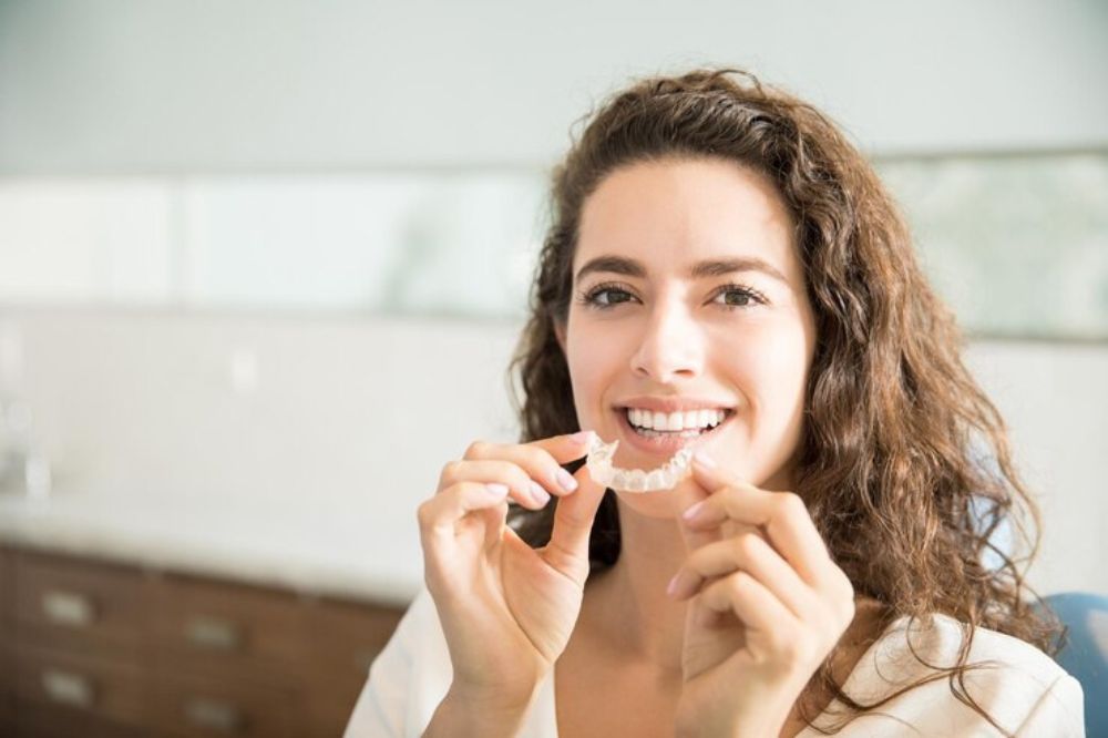 a lady is smiling and holding aligners